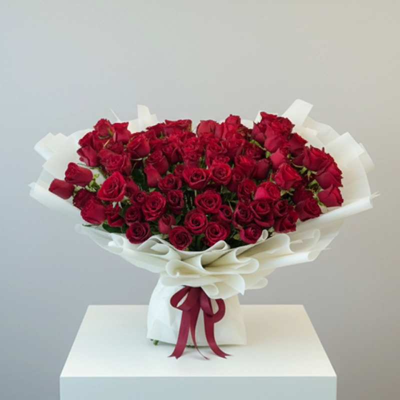 Large, luxurious bouquet of red spray roses (baby roses) wrapped in white paper with a red ribbon, a romantic gift for delivery in the UAE.